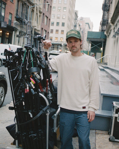 Man standing on a city street with film equipment, wearing Photosupply Cap and Baseline Thermal.